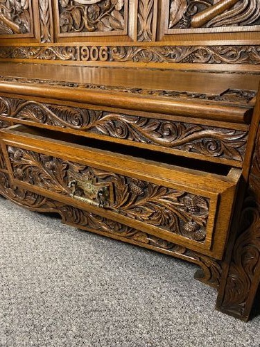 An Edwardian carved oak hall bench dated 1906, featuring mythological beast motifs, foliage panels, carved beast head armrests, and two lower drawers. View IV