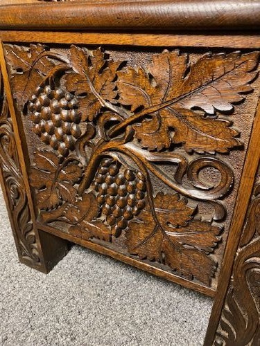 An Edwardian carved oak hall bench dated 1906, featuring mythological beast motifs, foliage panels, carved beast head armrests, and two lower drawers. View VIII