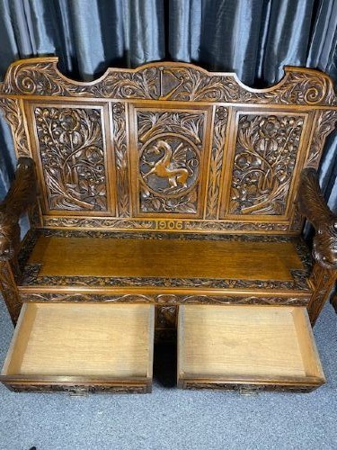 An Edwardian carved oak hall bench dated 1906, featuring mythological beast motifs, foliage panels, carved beast head armrests, and two lower drawers. View X