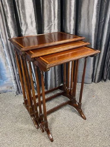 A set of three graduated mahogany nesting tables featuring light wood inlay borders on the rectangular tops and slender turned legs.