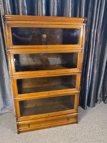 A four-tier warm brown oak barrister bookcase featuring glazed lift-and-slide doors and a single bottom drawer.
