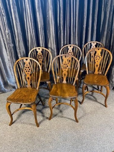 A set of six warm brown wooden Windsor dining chairs featuring hoop backs, pierced wheelback splats, shaped solid seats, and curved legs.