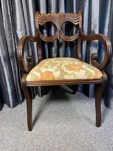 A carved mahogany carver armchair featuring reeded scroll arms, a sculpted double-circle back splat, and a floral upholstered seat.