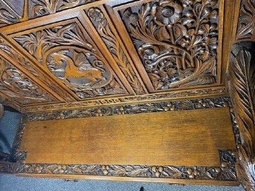 An Edwardian carved oak hall bench dated 1906, featuring mythological beast motifs, foliage panels, carved beast head armrests, and two lower drawers. View IX