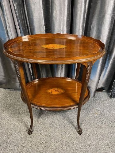 An oval two-tier mahogany occasional table featuring scalloped rims, central floral marquetry inlays, and slender cabriole legs with claw feet.