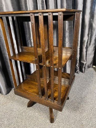 An antique dark oak revolving bookcase featuring a square top, vertical slatted sides, three open tiers, and a four-footed rotating base. View II