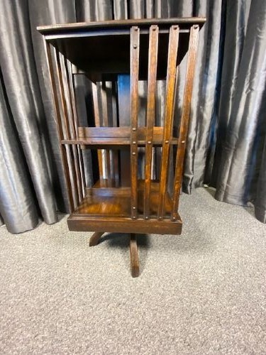 An antique dark oak revolving bookcase featuring a square top, vertical slatted sides, three open tiers, and a four-footed rotating base. View III
