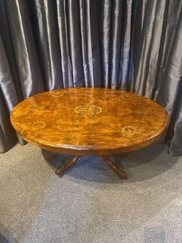 An oval burr walnut coffee table featuring detailed floral marquetry inlays on the tabletop and carved splayed legs.