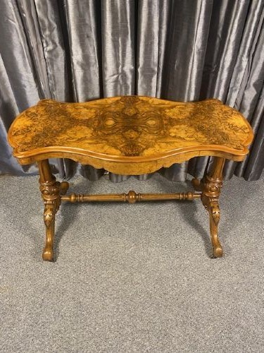 A Victorian burr walnut occasional table featuring a serpentine top with symmetrical book-matched grain, carved end-supports, and a central turned stretcher.