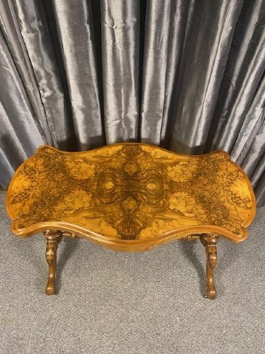 A Victorian burr walnut occasional table featuring a serpentine top with symmetrical book-matched grain, carved end-supports, and a central turned stretcher. View II