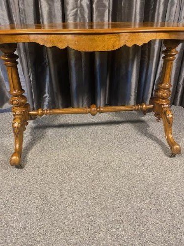 A Victorian burr walnut occasional table featuring a serpentine top with symmetrical book-matched grain, carved end-supports, and a central turned stretcher. View III