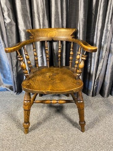 An antique oak captains chair featuring a curved horseshoe rail, turned wooden spindles, a contoured saddle seat, and turned legs with an H-stretcher.