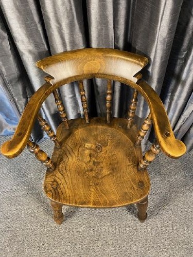 An antique oak captains chair featuring a curved horseshoe rail, turned wooden spindles, a contoured saddle seat, and turned legs with an H-stretcher. View II