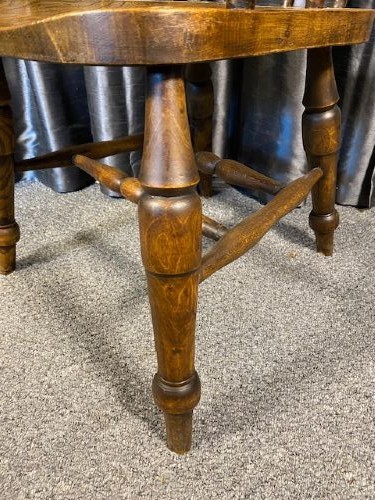 An antique oak captains chair featuring a curved horseshoe rail, turned wooden spindles, a contoured saddle seat, and turned legs with an H-stretcher. View III