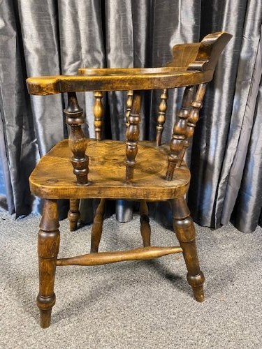 An antique oak captains chair featuring a curved horseshoe rail, turned wooden spindles, a contoured saddle seat, and turned legs with an H-stretcher. View IV