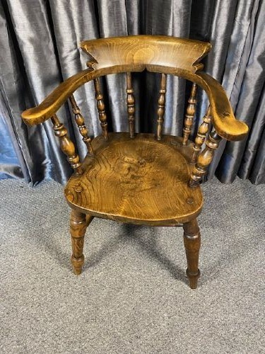 An antique oak captains chair featuring a curved horseshoe rail, turned wooden spindles, a contoured saddle seat, and turned legs with an H-stretcher. View V