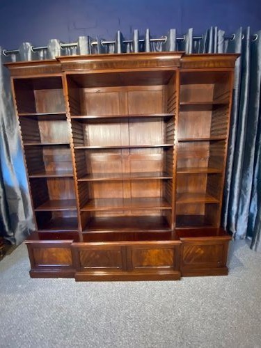 A large mahogany breakfront bookcase featuring a projecting central section with adjustable open shelves above a solid wooden plinth base.