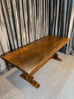 A solid oak refectory dining table with a rectangular top and carved end trestles connected by a low central stretcher rail. View II