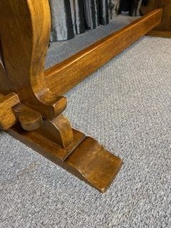 A solid oak refectory dining table with a rectangular top and carved end trestles connected by a low central stretcher rail. View V