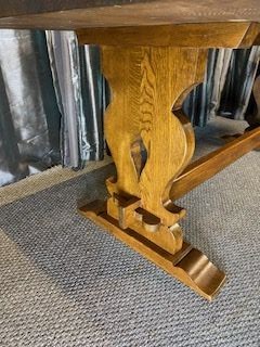 A solid oak refectory dining table with a rectangular top and carved end trestles connected by a low central stretcher rail. View VII