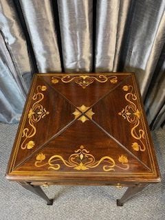 An Edwardian mahogany envelope card table featuring floral marquetry inlay on four folding flaps, a single drawer with brass knobs, and square tapered legs. View V