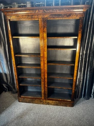 A large double-bay open bookcase made of burr walnut veneer with a moulded top cornice and dark interior shelving.