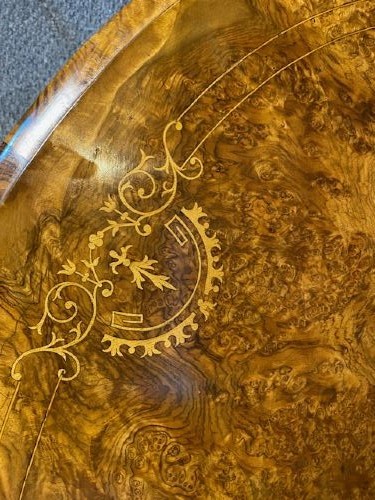 An oval burr walnut coffee table featuring floral marquetry inlay, a moulded rim, and carved splayed legs. View IV