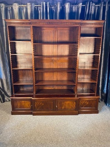 A large Victorian mahogany open breakfront bookcase featuring three sectioned shelving units over a low plinth cabinet base.