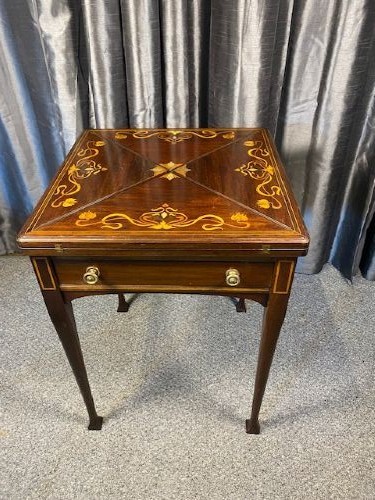 An Edwardian mahogany envelope card table featuring marquetry floral inlay on four triangular folding top leaves, a single drawer with brass handles, and square tapered legs. View II