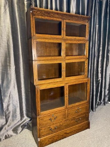 A tall golden oak barrister bookcase featuring four stacked glazed compartments over a base unit with drawers. View II