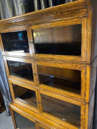 A tall golden oak barrister bookcase featuring four stacked glazed compartments over a base unit with drawers. View III
