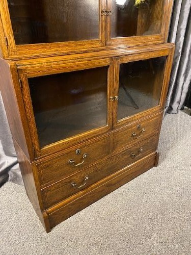 A tall golden oak barrister bookcase featuring four stacked glazed compartments over a base unit with drawers. View IV