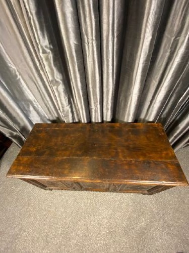 A dark oak coffer featuring three carved lozenge panels, a carved top rail, turned stiles, and a hinged rectangular top. View II