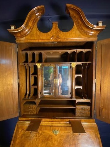 An antique walnut bureau bookcase featuring a broken arch pediment, double mirrored cabinet doors, a slant-front writing slope, and several drawers with brass handles. View XIII
