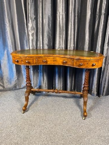 An antique kidney-shaped walnut writing desk featuring an inset green leather writing surface, frieze drawers, turned legs, and a stretcher base. View V