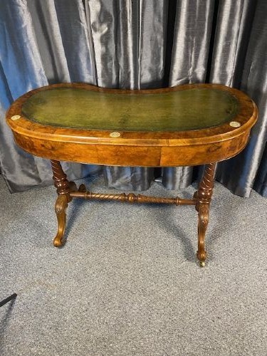 An antique kidney-shaped walnut writing desk featuring an inset green leather writing surface, frieze drawers, turned legs, and a stretcher base. View VI