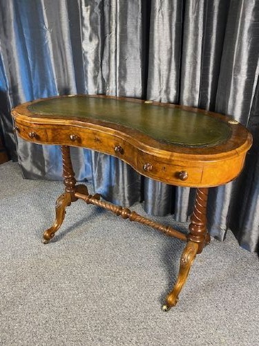 An antique kidney-shaped walnut writing desk featuring an inset green leather writing surface, frieze drawers, turned legs, and a stretcher base. View VII