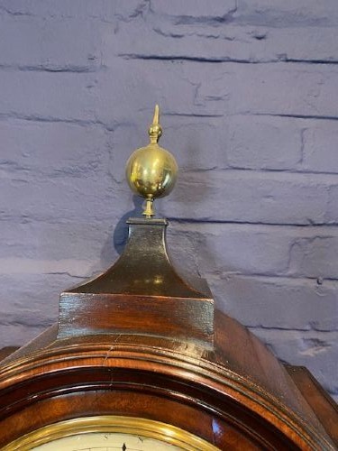 A tall flame mahogany longcase clock with an arched hood, brass finial, and round dial face. View III