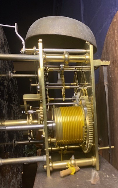 A tall flame mahogany longcase clock with an arched hood, brass finial, and round dial face. View VII