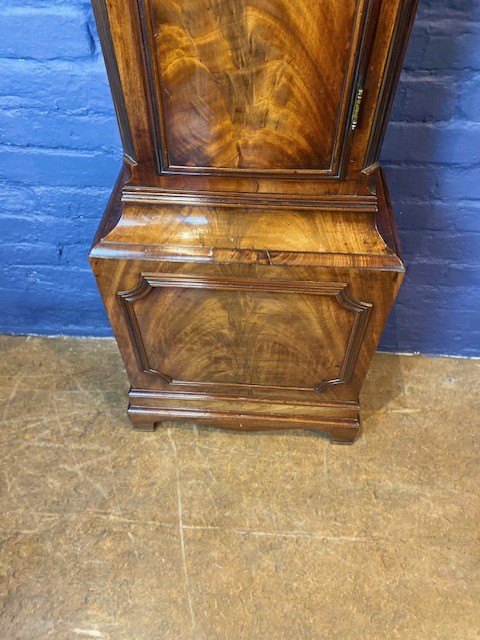 A tall flame mahogany longcase clock with an arched hood, brass finial, and round dial face. View IX