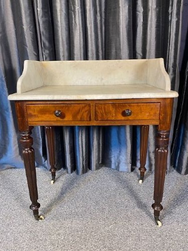 A Victorian mahogany washstand featuring a white marble top with splashback, twin drawers, and turned reeded legs on brass castors.