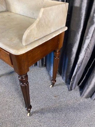 A Victorian mahogany washstand featuring a white marble top with splashback, twin drawers, and turned reeded legs on brass castors. View II