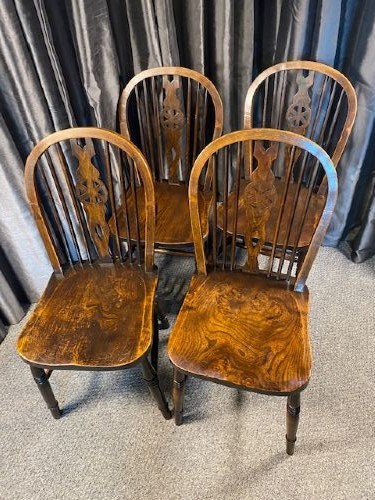 A set of four antique English country Windsor dining chairs featuring hoop backs, wheelback central splats, shaped elm seats, and turned legs.