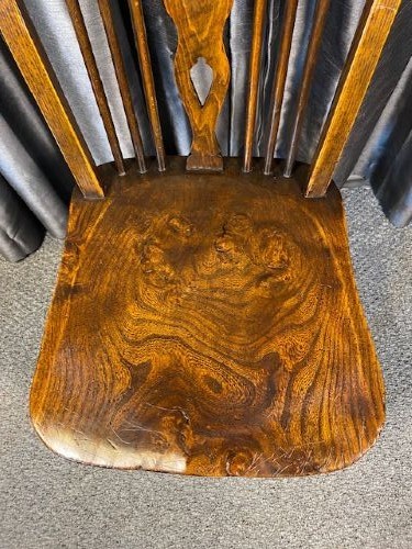 A set of four antique English country Windsor dining chairs featuring hoop backs, wheelback central splats, shaped elm seats, and turned legs. View IV
