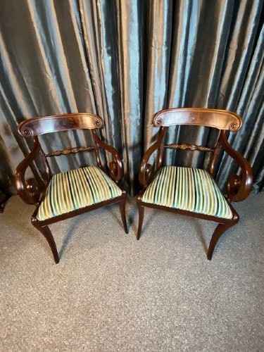 A pair of antique Regency mahogany carver chairs featuring curved scroll arms, carved crossbars, striped fabric upholstered seats, and sabre legs.