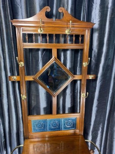 A tall walnut hall stand featuring a top scrolled crest, brass hooks, a diamond-shaped central mirror, blue ceramic tiles, a glove drawer, and umbrella holders with drip trays. View II