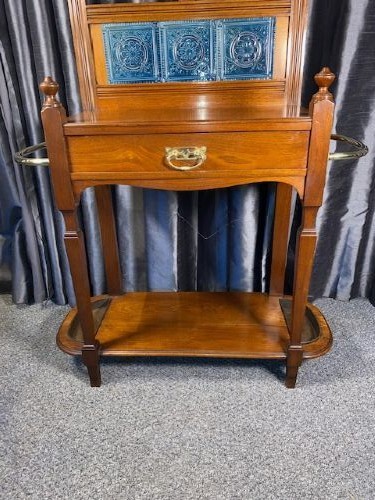 A tall walnut hall stand featuring a top scrolled crest, brass hooks, a diamond-shaped central mirror, blue ceramic tiles, a glove drawer, and umbrella holders with drip trays. View V