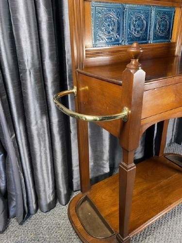 A tall walnut hall stand featuring a top scrolled crest, brass hooks, a diamond-shaped central mirror, blue ceramic tiles, a glove drawer, and umbrella holders with drip trays. View VI