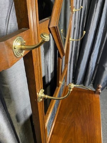 A tall walnut hall stand featuring a top scrolled crest, brass hooks, a diamond-shaped central mirror, blue ceramic tiles, a glove drawer, and umbrella holders with drip trays. View VII
