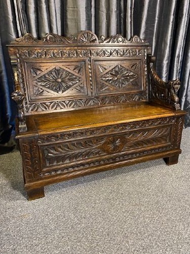 A dark carved oak storage bench featuring a high backrest with geometric floral panels and a enclosed box seat base.